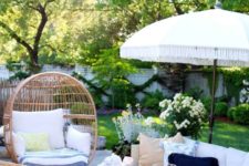 a small and cozy summer patio with neutral furniture, wicker chairs, printed textiles, baskets and a white umbrella over the space