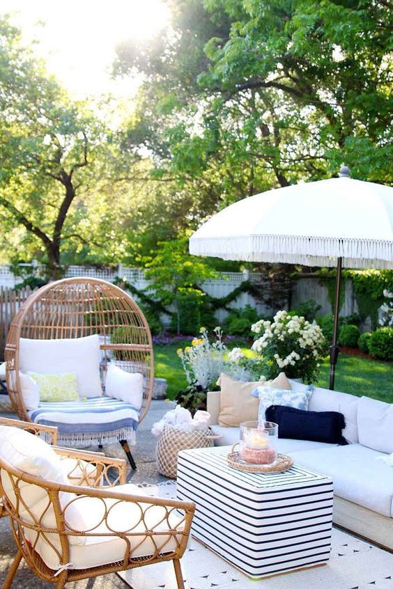a small and cozy summer patio with neutral furniture, wicker chairs, printed textiles, baskets and a white umbrella over the space