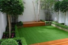 a small and elegant garden with a green lawn, with some flower beds with blooms and greenery and shrubs and trees