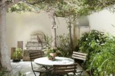 a small and elegant patio with lots of greenery, a stone deck, a small dining set, a tree and some wood decor