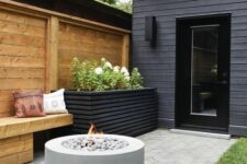 a small and laconic patio with a wooden bench, a tall black planter with greenery and blooms and a fire pit is a cool space