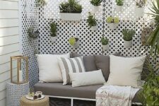 a small and lovely patio with a trellis holding planters with greenery, a grey sofa with pillows, a candle lantern and some baskets