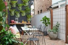 a small and lovely patio with potted greenery, a bar counter, a wooden table and black chairs and some string lights over the space