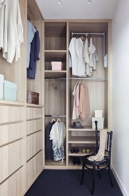 A small and narrow walk in closet with light stained drawers, open storage compartments and railings, a black vintage chair