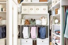 a small and stylish white closet with built-in shelves and drawers, boxes for shoes and hats and a large mirror on the wall