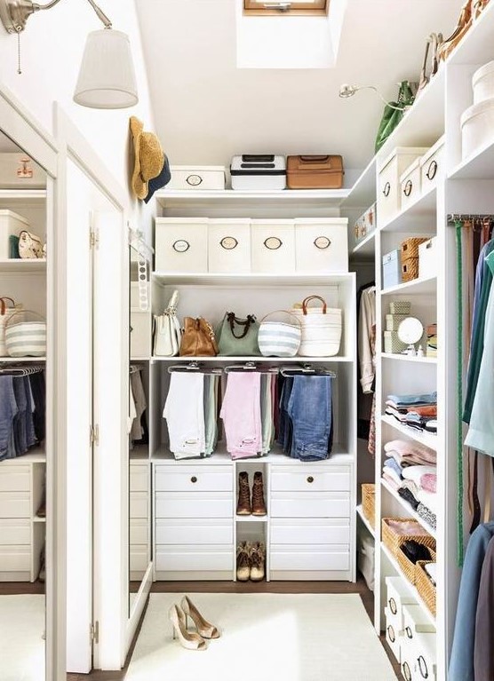 A small and stylish white closet with built in shelves and drawers, boxes for shoes and hats and a large mirror on the wall
