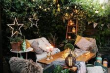 a small and welcoming patio with a greenery wall, a wooden table, chairs, a sofa, some printed textilesm candles and candle lanterns