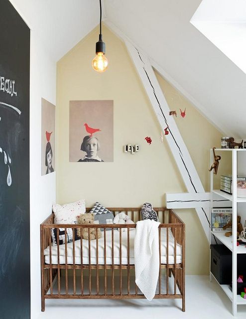a small attic nursery with a catchy artwork, a chalkboard door, a simple crib and a storage unit for a modern look