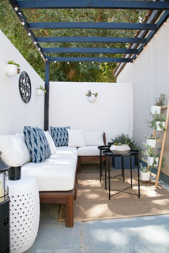 a small backyard with walls, string lights, a large corner sofa, black coffee tables, potted greenery and side tables