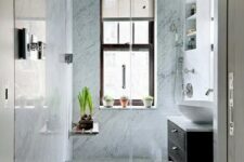 a small bathroom with blue stone tiles in the shower, a dark stained vanity, potted greenery and built-in shelves