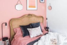 a small bedroom with a pink accent wall, a bed with a cane headboard and pink and black bedding, a gallery wall and mirror faceted nightstands