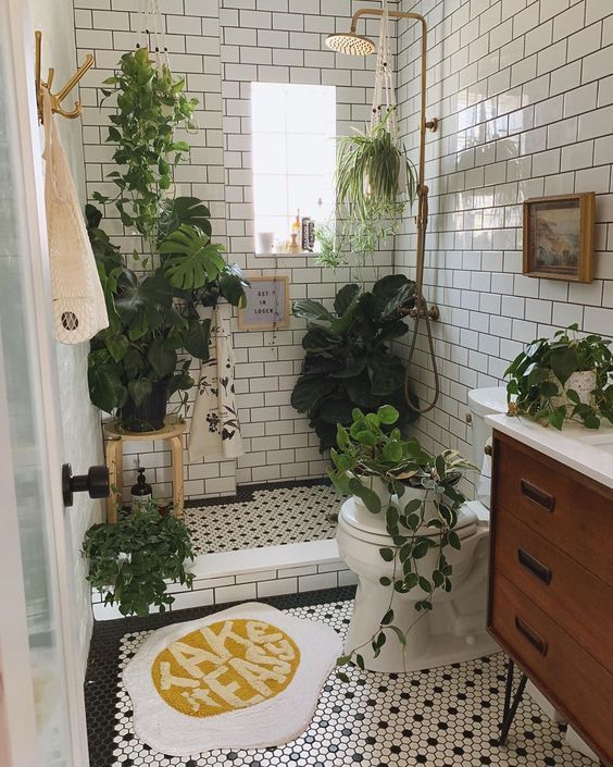 a small boho bathroom clad with white subway tiles, with black and white penny ones, with lots of plants for a forest feel