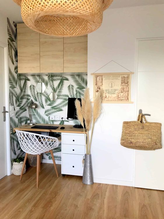 a small boho tropical home office nook with a tropical wall, a white chair, pampas grass, a wicker lamp and an artwork