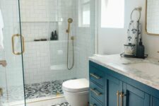 a small bright bathroom with white tiles in the shower, printed tiles on the floor, a navy vanity and brass fixtures