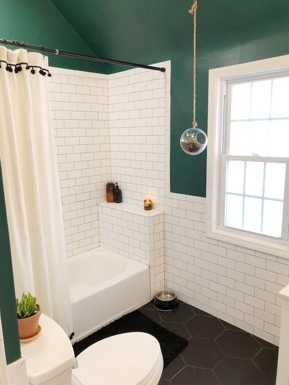 a small catchy bathroom with dark green walls and a ceiling, white subway tiles, black hex ones, a shower space and a window