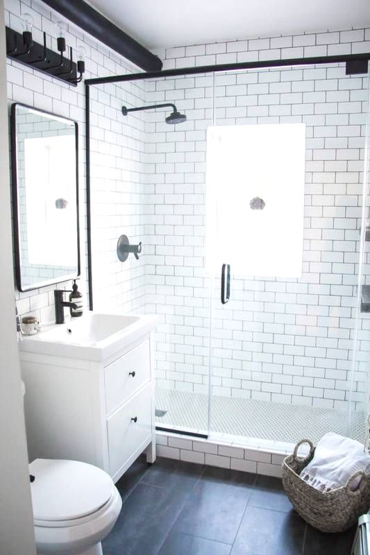 a small contemporary bathroom with white subway tiles, black tiles on the floor, a tiny vanity and black fixtures