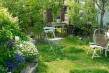 a small garden with a lawn, a flower bed with bright blooms, some vintage garden furniture and some shrubs and trees