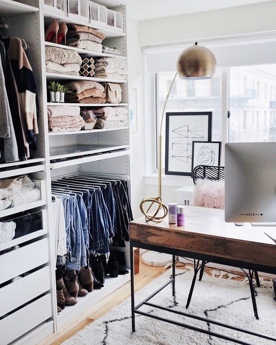 a small glam cloffice with a large makeshift closet, a stylish wood and metal desk, artworks and a catchy brass lamp