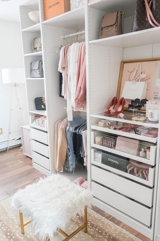 A small glam closet with holders and hangers, built in drawers, open shelving, artworks, a faux fur stool and a printed rug