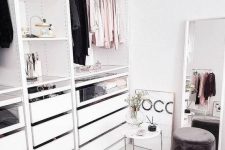 a small glam closet with shelves, a holder for hangers and some drawers, a large window and a cute suede ottoman
