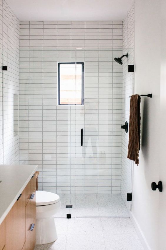 a small minimalist bathroom with neutral tiles, with skinny ones and printed ones on the floor, a small window and black fixtures for a modern feel