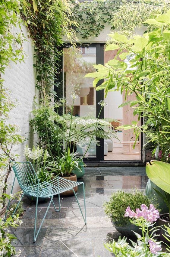 a small modern patio with a tiled floor, a green metal chair, some potted plants and blooms is a cool and laconic space