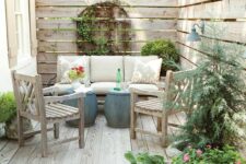 a small patio with a sofa, wooden chairs, mini side tables, potted greenery and blooms is a cozy rustic nook