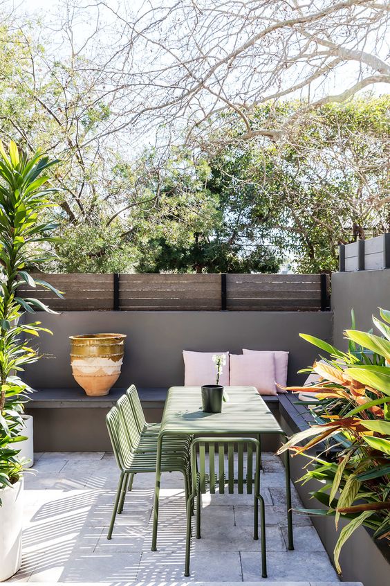 A small patio with a tile floor, a corner built in bench, lots of potted greenery around and a dining set