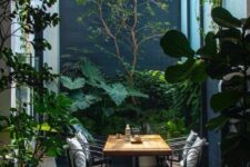 a small patio with a tiled floor, a wooden table and forged chairs, lots of greenery around is perfect for having meals