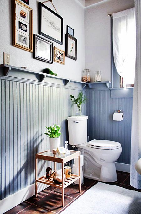 a small powder room with powder blue beadboard, a window, a gallery wall and some dark tiles on the floor