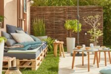 a small rustic summer terrace with a tiled space, a pallet sofa, wooden stools and potted greenery and candle lanterns