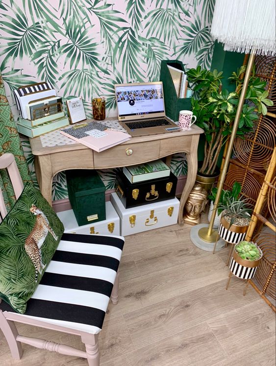 a small tropical home office with an accent wall, a rattan screen, gold planters, various boxes, tropical pillows and touches of brass