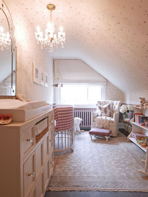 A small vintage inspired attic nursery with a crystal chandelier, a large dresser, some furniture for the kid and adults