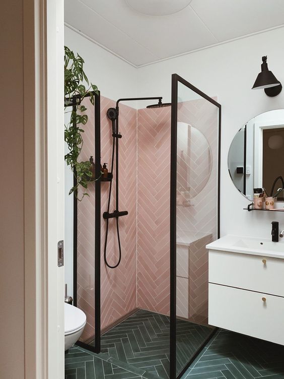 a small yet catchy bathroom with pink herringbone tiles and grene ones, a white vanity and black fixtures here and there