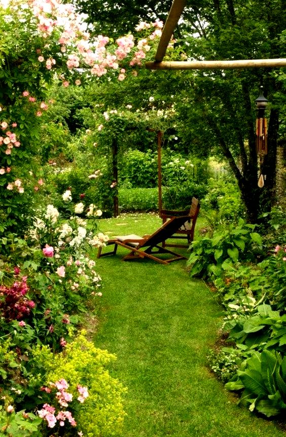 a small yet very lush garden with a manicured lawn, greenery, pink flowers and an arch with climbing greenery and blooms