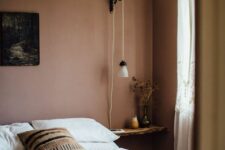 a soothing bedroom with mauve walls, a bed with neutral bedding, a floating nightstand and some lamps and lights