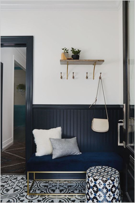 a stylish entryway with midnight blue beadboard, a navy bench, printed tiles on the floor and a bright printed ottoman