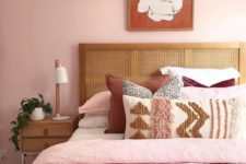 a stylish modern bedroom with light pink walls, pink, neutral and burgundy bedding, wooden furniture and a statement artwork