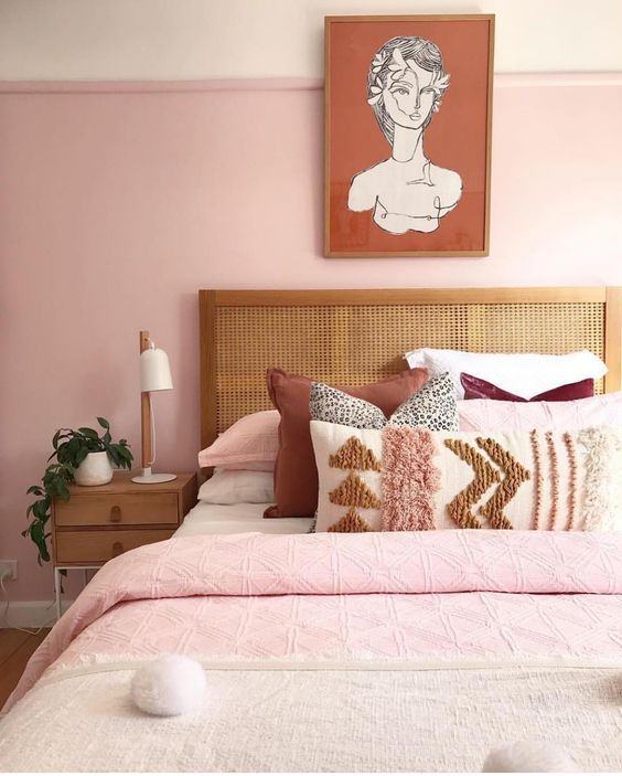 a stylish modern bedroom with light pink walls, pink, neutral and burgundy bedding, wooden furniture and a statement artwork