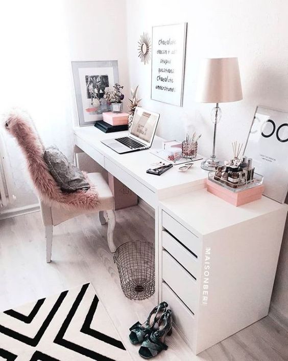 a stylish monochromatic home office with a faux fur cover, pink accessories and a pink lamp plus a graphic rug