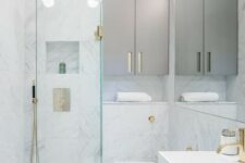 a tiny minimalist bathroom with white marble tiles, sleek grey cabinets, gilded touches and a triangle shower space