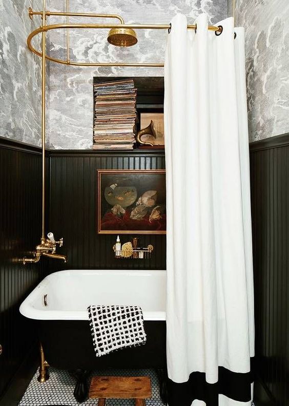 A vintage inspired bathroom done with wallpaper and black beadboard, a black tub, vintage books and artworks