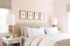 a welcoming modern bedroom with light pink walls, a neutral bed, a wicker lamp and white furniture and a gallery wall