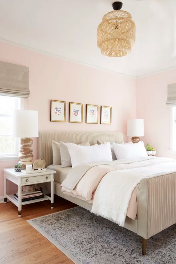 a welcoming modern bedroom with light pink walls, a neutral bed, a wicker lamp and white furniture and a gallery wall