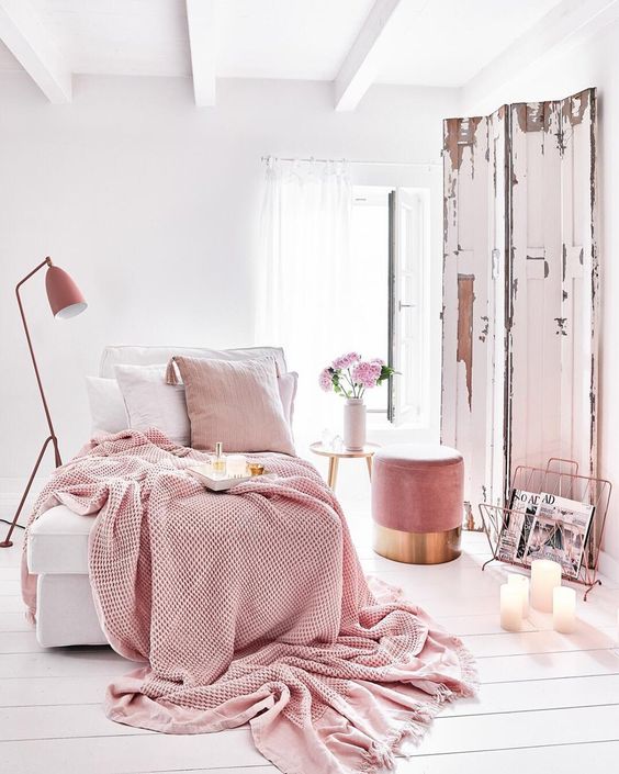 a welcoming white bedroom with a pink ottoman, pink and white bedding, a pink lamp and magazine stand is wow