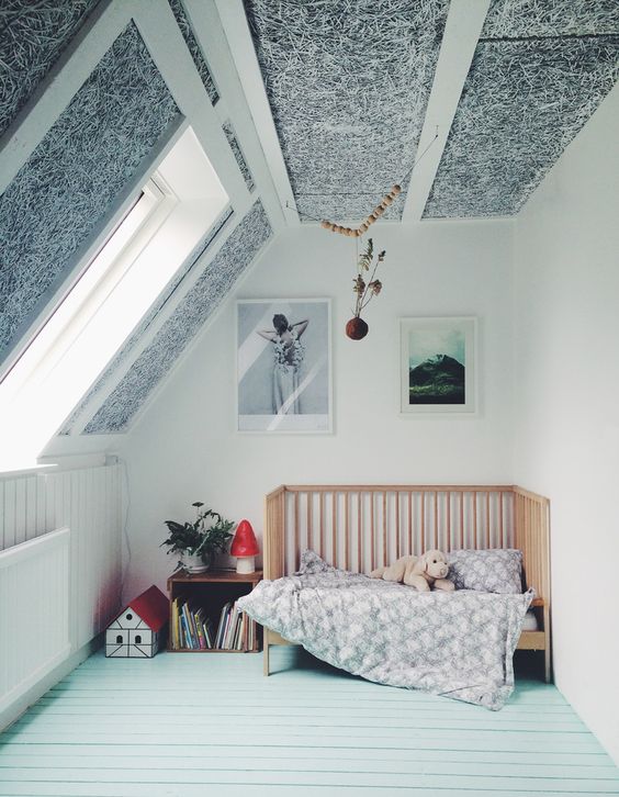 an attic nursery with a mint floor, a black and white paneled ceiling, a crib and some toys and storage units
