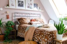 an attic pink boho bedroom with a ledge gallery wall, a metal bed with printed bedding, layered rugs, potted greenery and a lantern