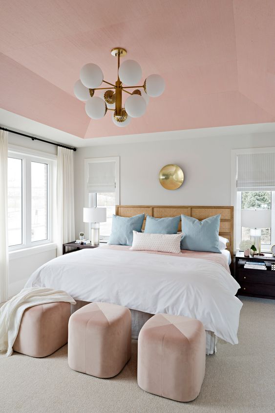 an elegant modern bedroom with a pink ceiling and color block ottomans, blue pillows and touches of gold