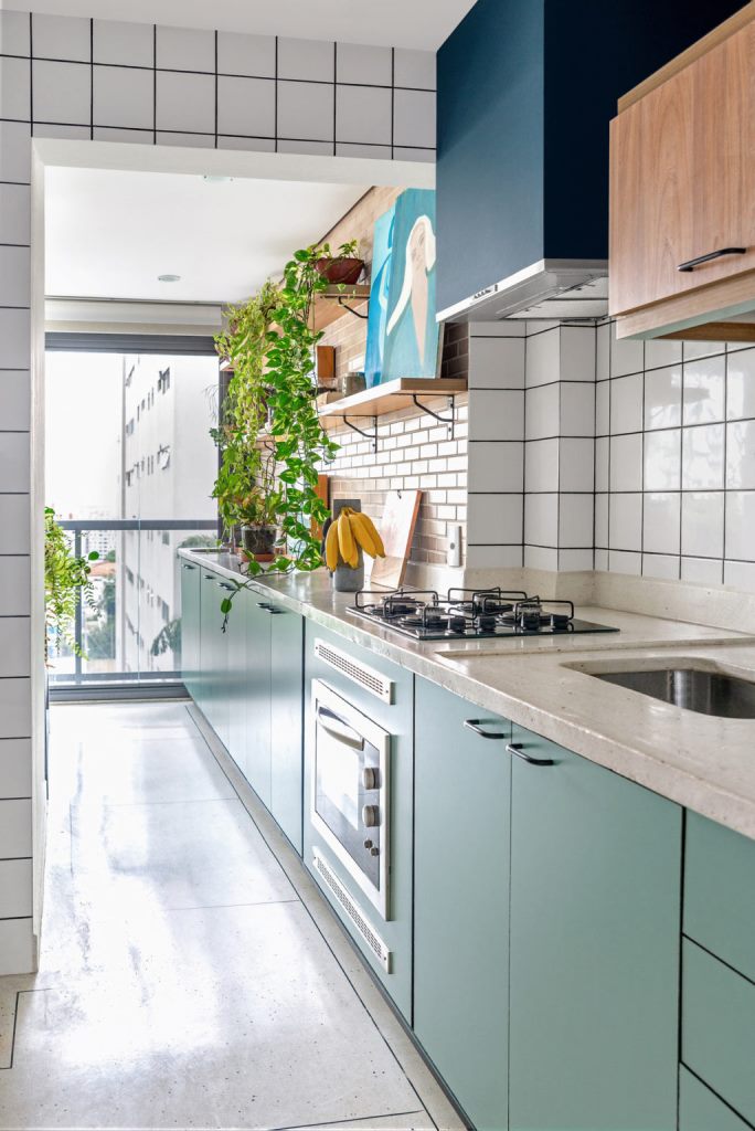 The kitchen is long and narrow, done with green cabinets, white terrazzo countertops, blush and white tile backsplashes