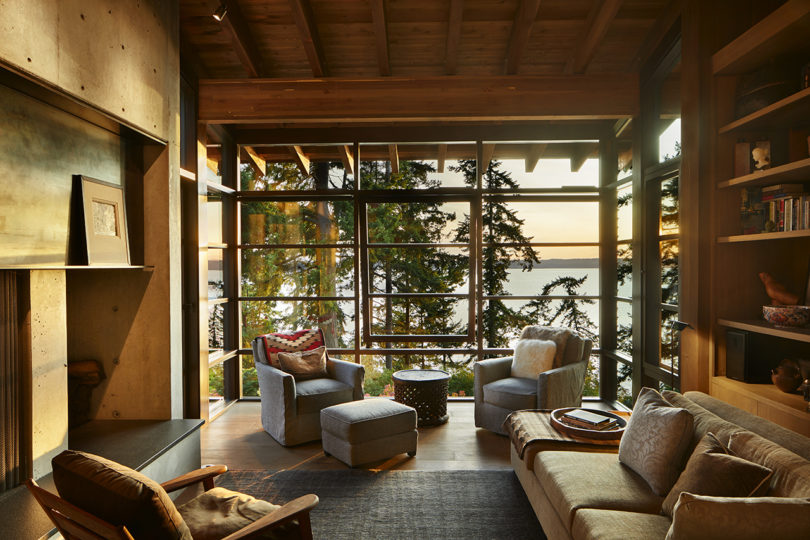 The living room shows off a glazed wall with forest and coastal views, a built in fireplace and modern furniture